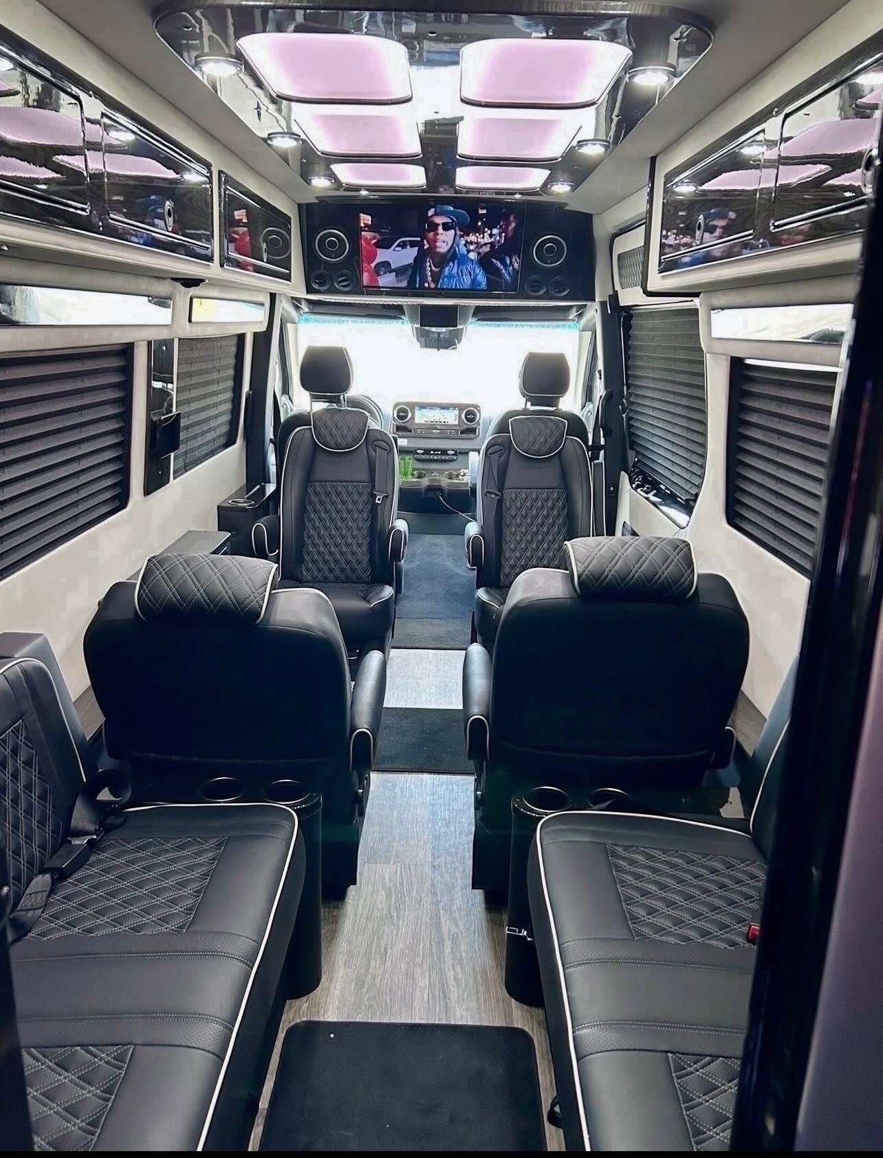 Luxury van interior with quilted black seats, ceiling lights, and TV screens