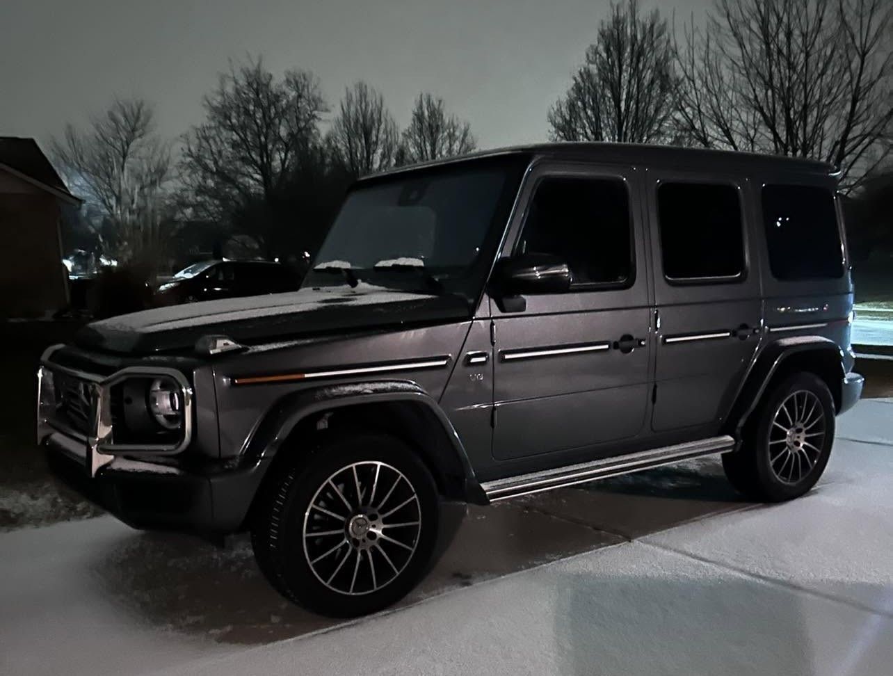 Dark gray Mercedes G-Class SUV parked on a snowy driveway at night