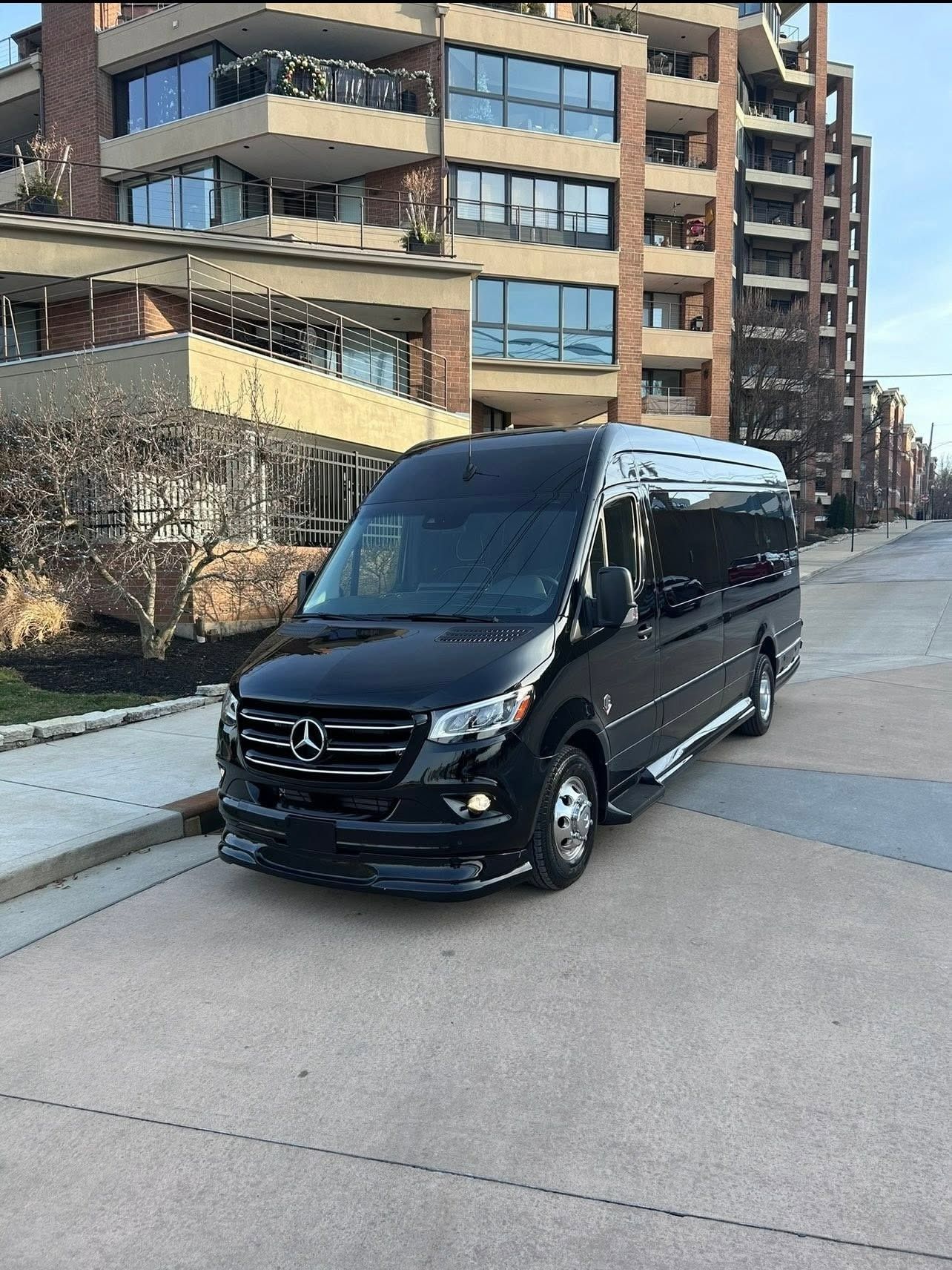 Black Mercedes van parked on a street beside apartment buildings on a sunny day