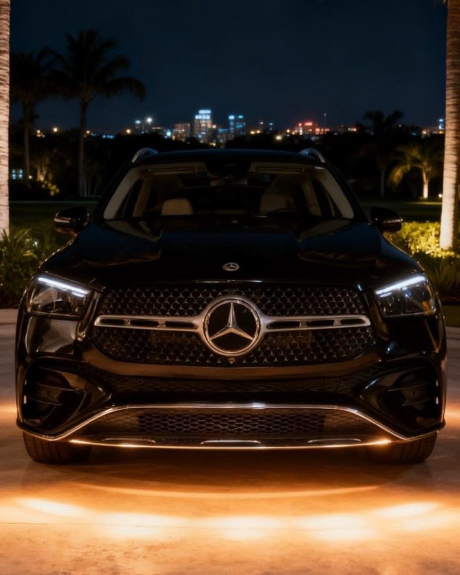 Black Mercedes SUV parked at night, front view with city lights in the background and warm underglow lighting.