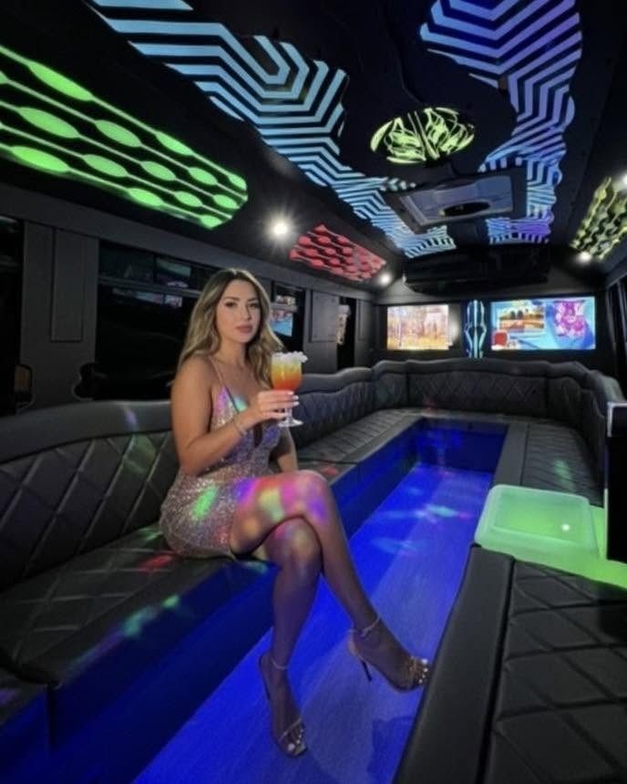 Woman seated in a neon-lit limousine, holding a drink beside a glowing blue center table.