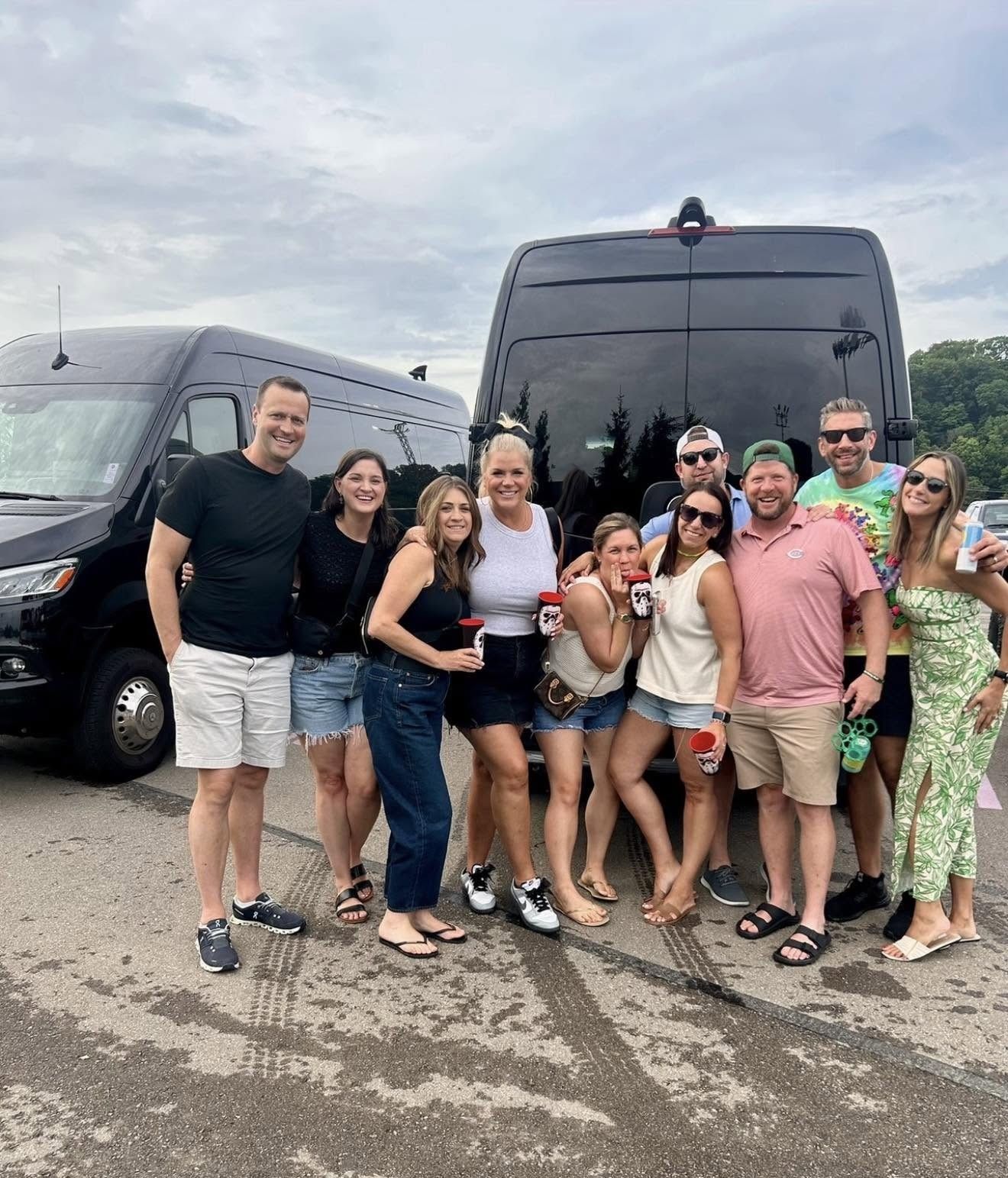 Group posing in front of two black tour buses in a parking lot, smiling and standing close together.