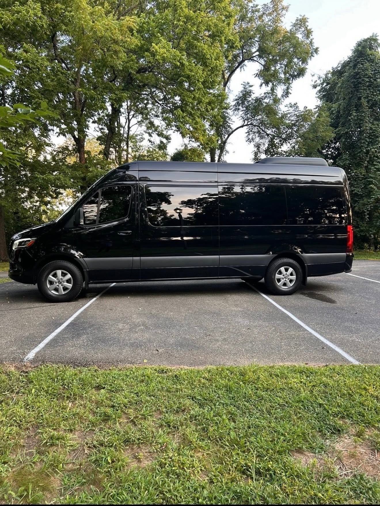 Black van parked in a gravel lot between white lines, with trees in the background.