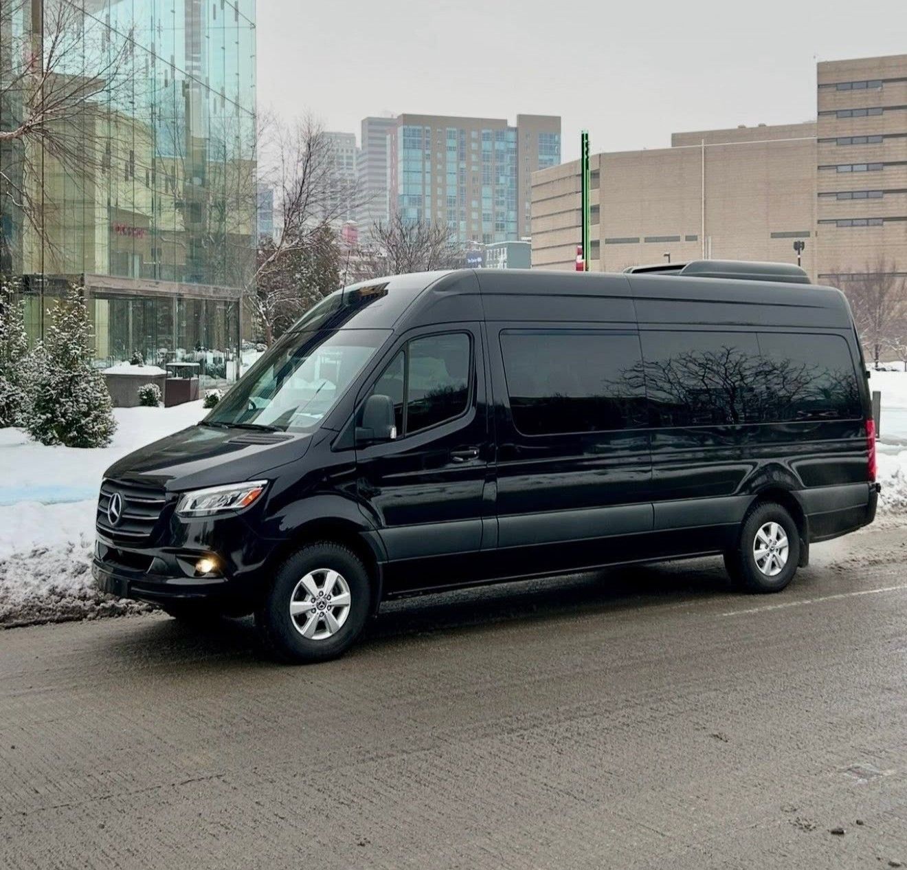 Black passenger van parked on a snowy street beside modern buildings