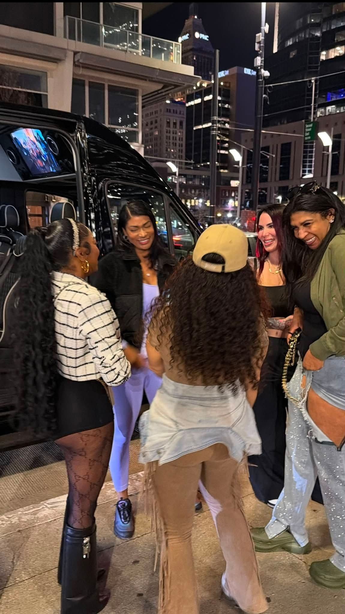 Group of friends standing and dancing on a city street at night, with lit buildings in the background