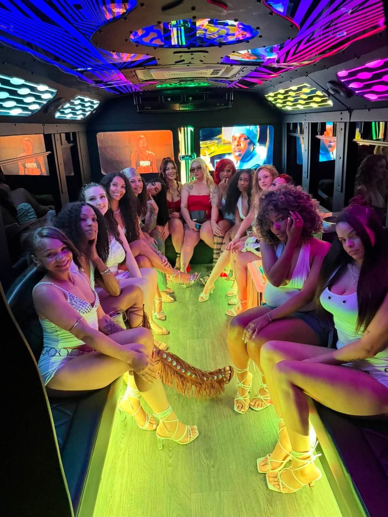 Group seated around a neon-lit table on a party bus, smiling and raising drinks