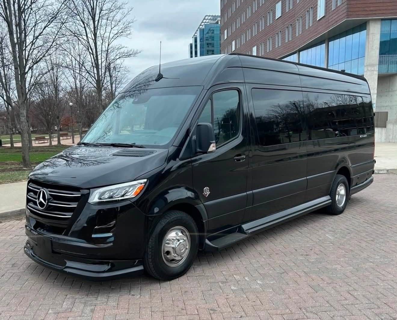 Black Mercedes minibus parked beside a modern building on a paved street.