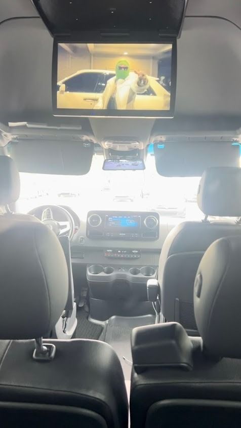 Rear-seat view of a car interior with a ceiling-mounted screen showing a movie scene.