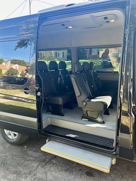 Black passenger van with sliding door open, showing rows of seats and a deployed step ramp.