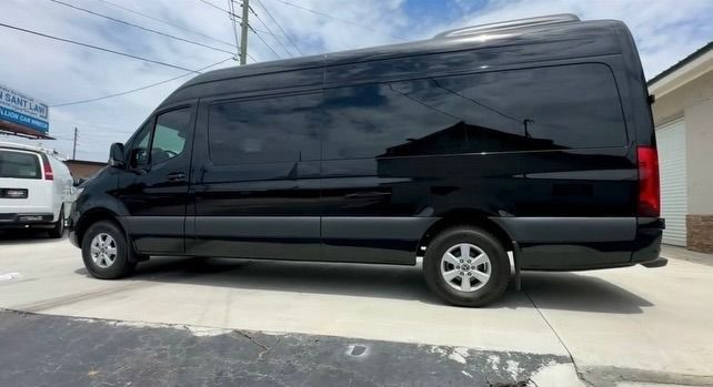 Black cargo van parked in a lot under a bright sky, side view