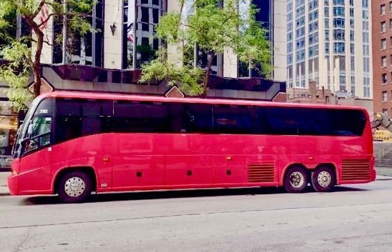 Bright red luxury coach bus parked on a city street beside tall buildings