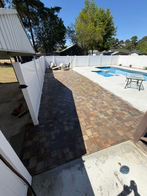 Backyard patio with brick walkway, white fence, pool cover, and lounge chair in bright sunlight