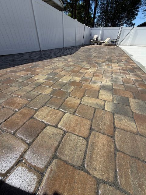 Stone-paved outdoor walkway beside white fences in bright sunlight