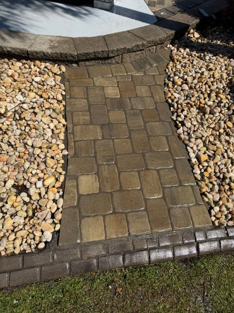 Stone paver walkway bordered by white pebbles and brown bricks beside a curved planter.