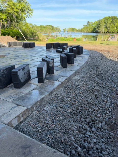 Outdoor riverside memorial with black stone seats on a paved platform beside gravel and trees