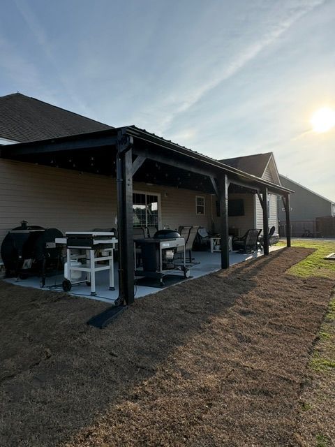 Covered patio with grill, table, and chairs beside a house at sunset