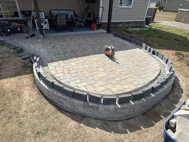Circular stone patio with curved retaining wall in a backyard, paved center and lawn around it