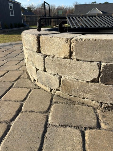 Stone fire pit in a paved courtyard, with a black metal railing and roofed structure in the background