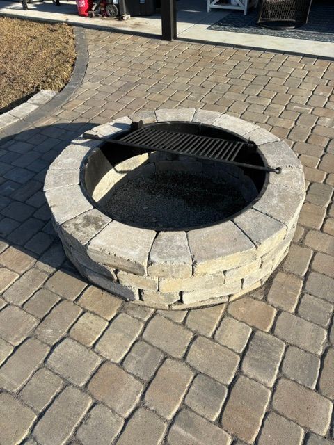 Stone circular fire pit set into a paved courtyard, with a metal grate across the opening.