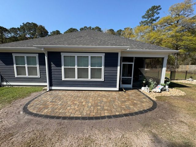 Front view of a blue house with a brick patio and small covered porch under a bright sky