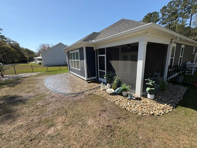 Corner of a single-story house with screened porch, gravel path, and small landscaped garden