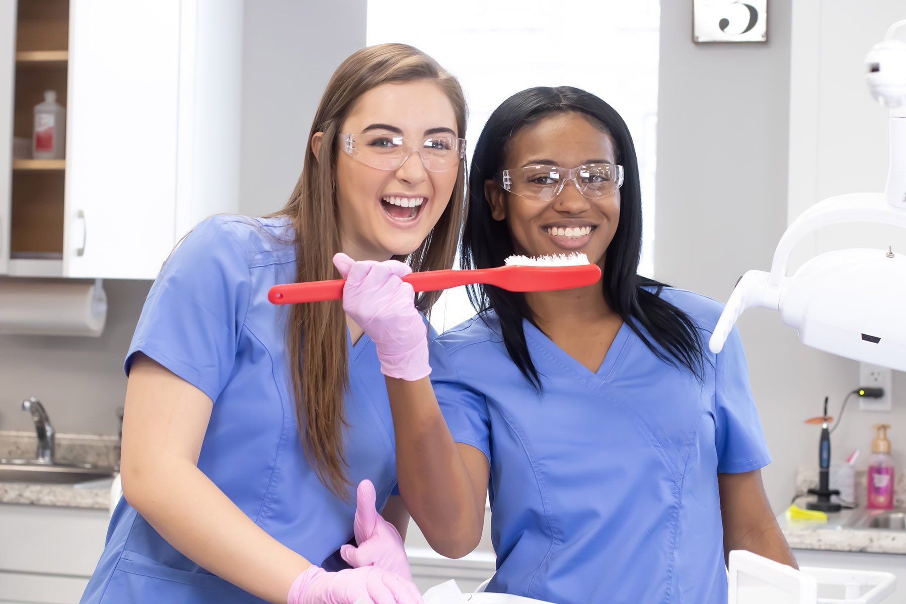 Two female dentists are brushing their teeth together in a dental office.