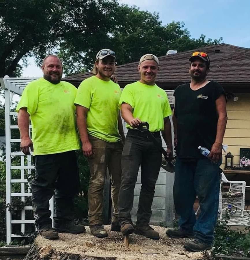 Four men stand outdoors in neon shirts, posing together by a house and white trellis.
