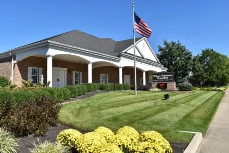 Brick civic building with white columns, American flag, and landscaped lawn under a clear blue sky