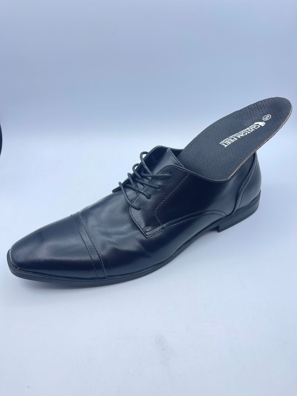 A pair of black shoes with a black insole on a white surface.