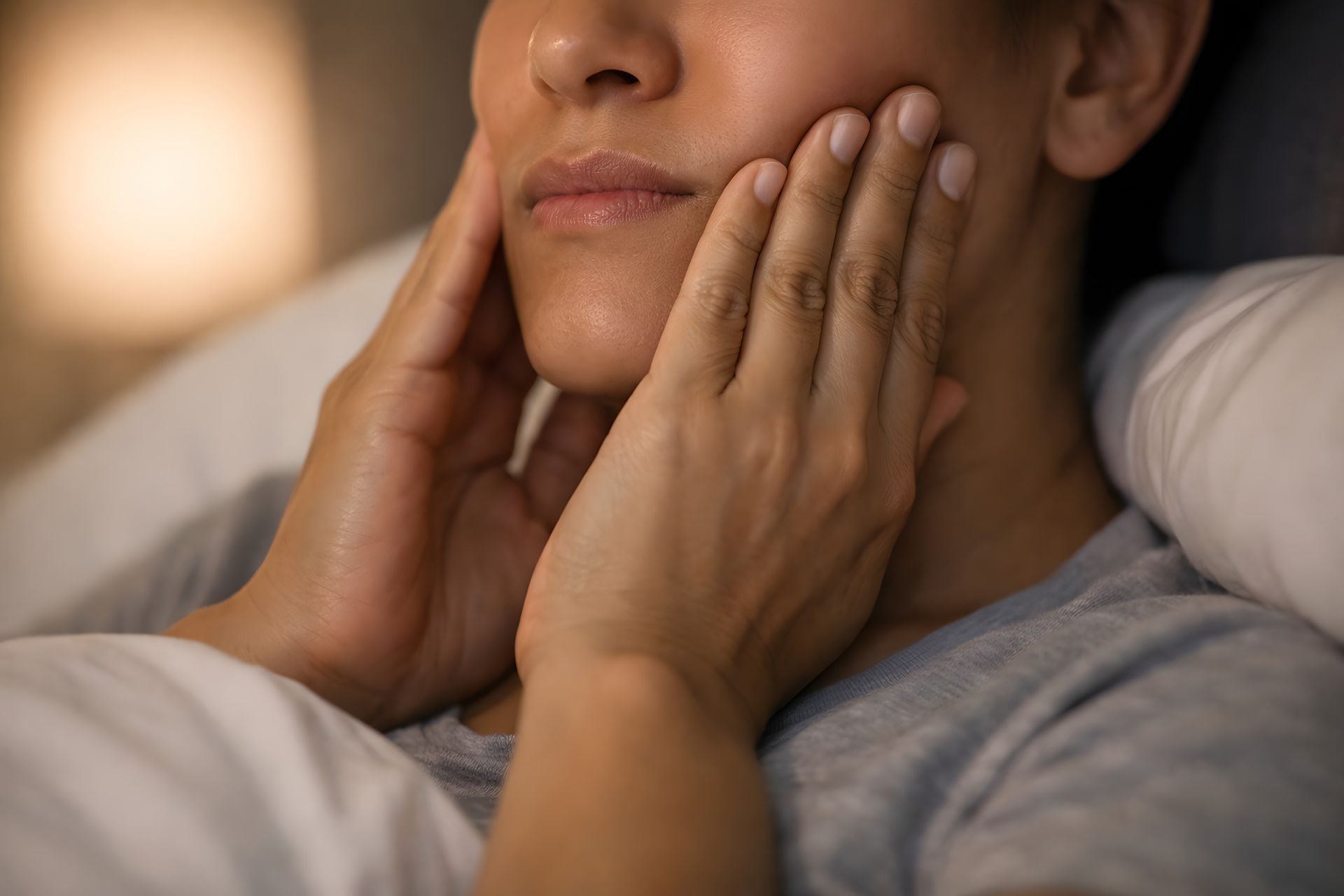 Hands gently holding a person’s face while they rest in bed