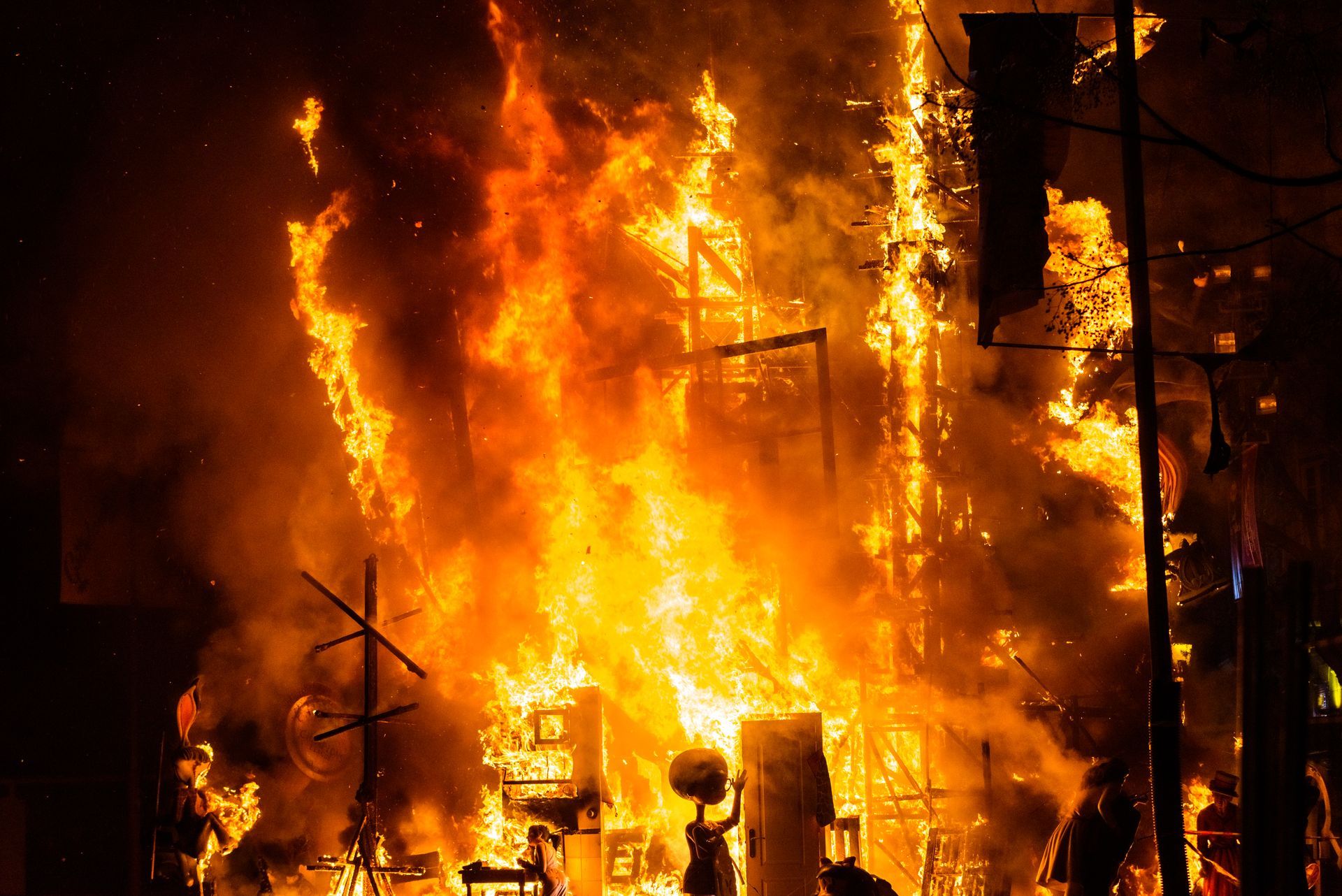 Building engulfed in flames, bright orange and yellow fire against a dark background.