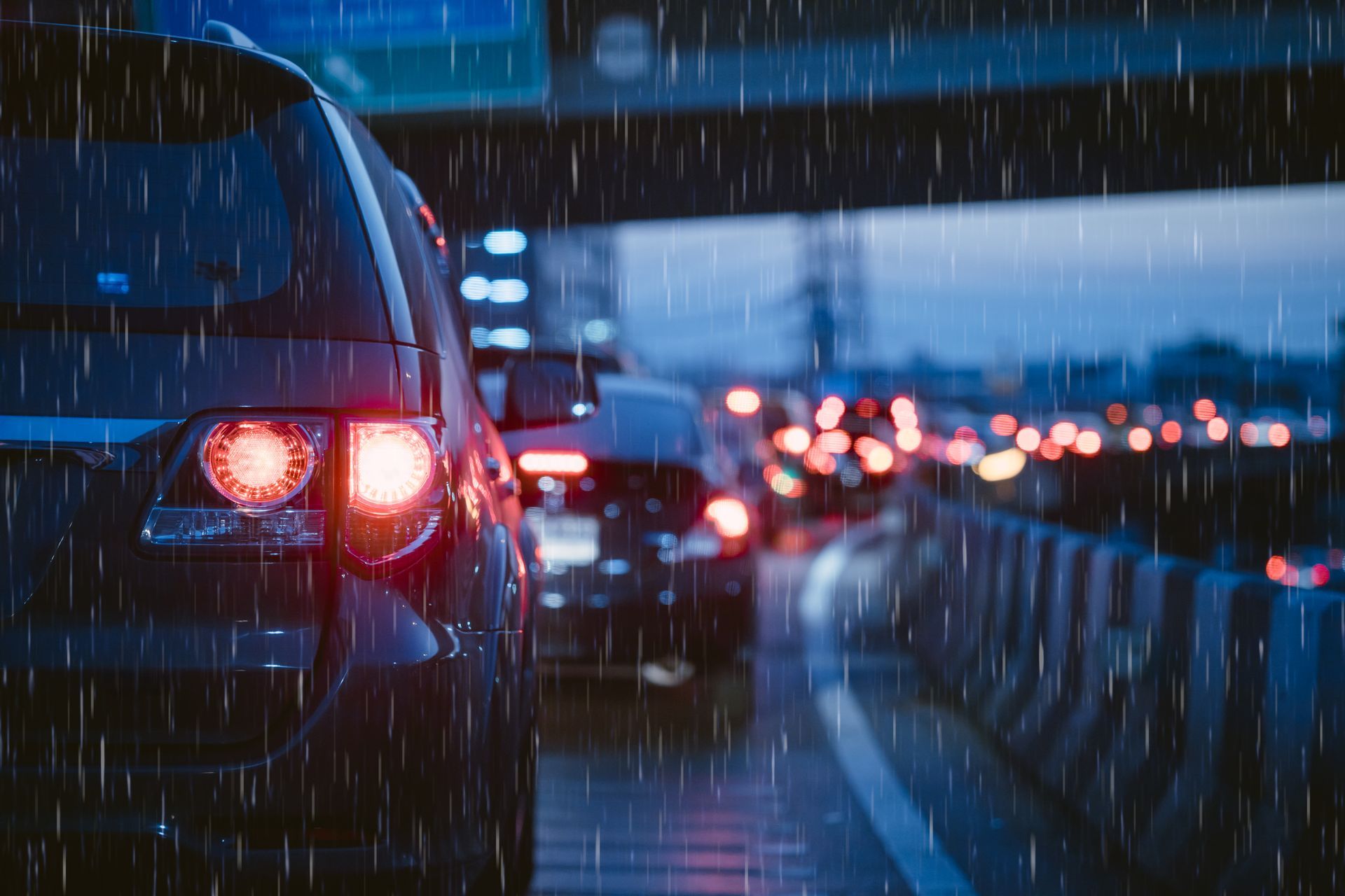 Cars in traffic on a wet highway at night; rain falling, taillights illuminated.