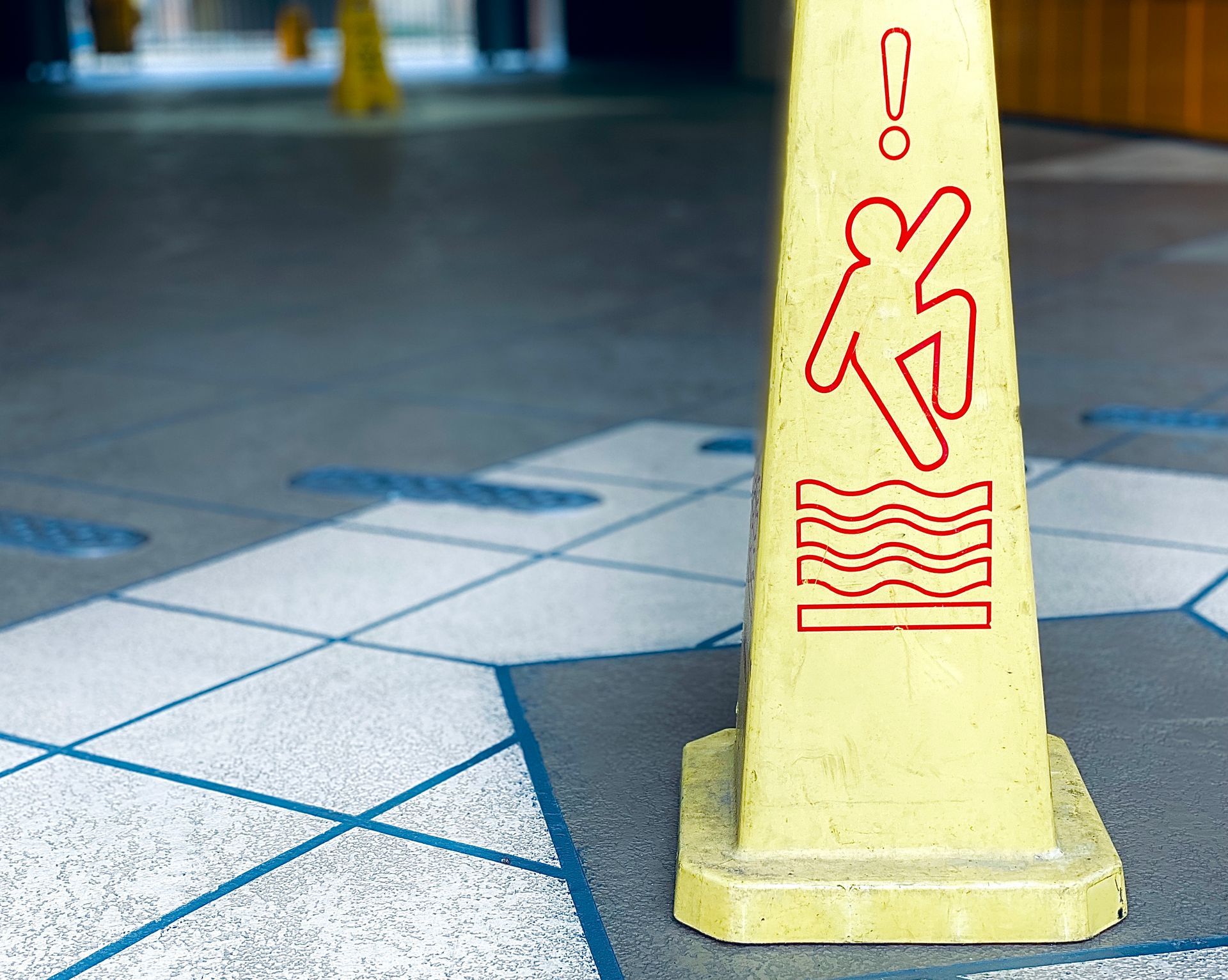 Yellow wet floor cone on tiled floor, warning of slippery surface.