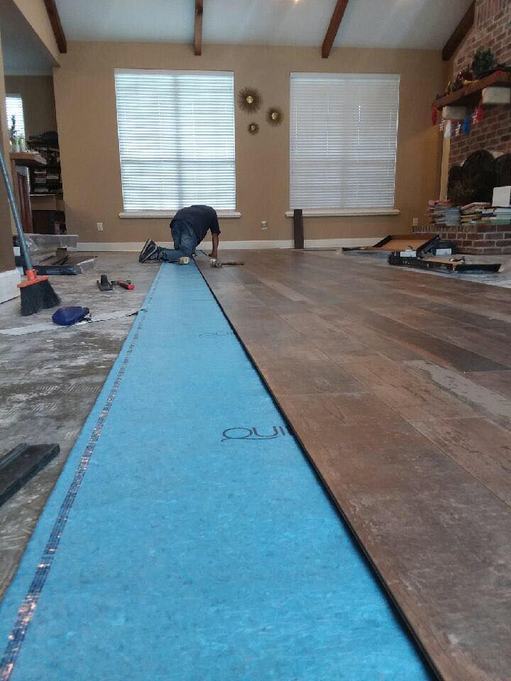 A man is laying a wooden floor in a living room.