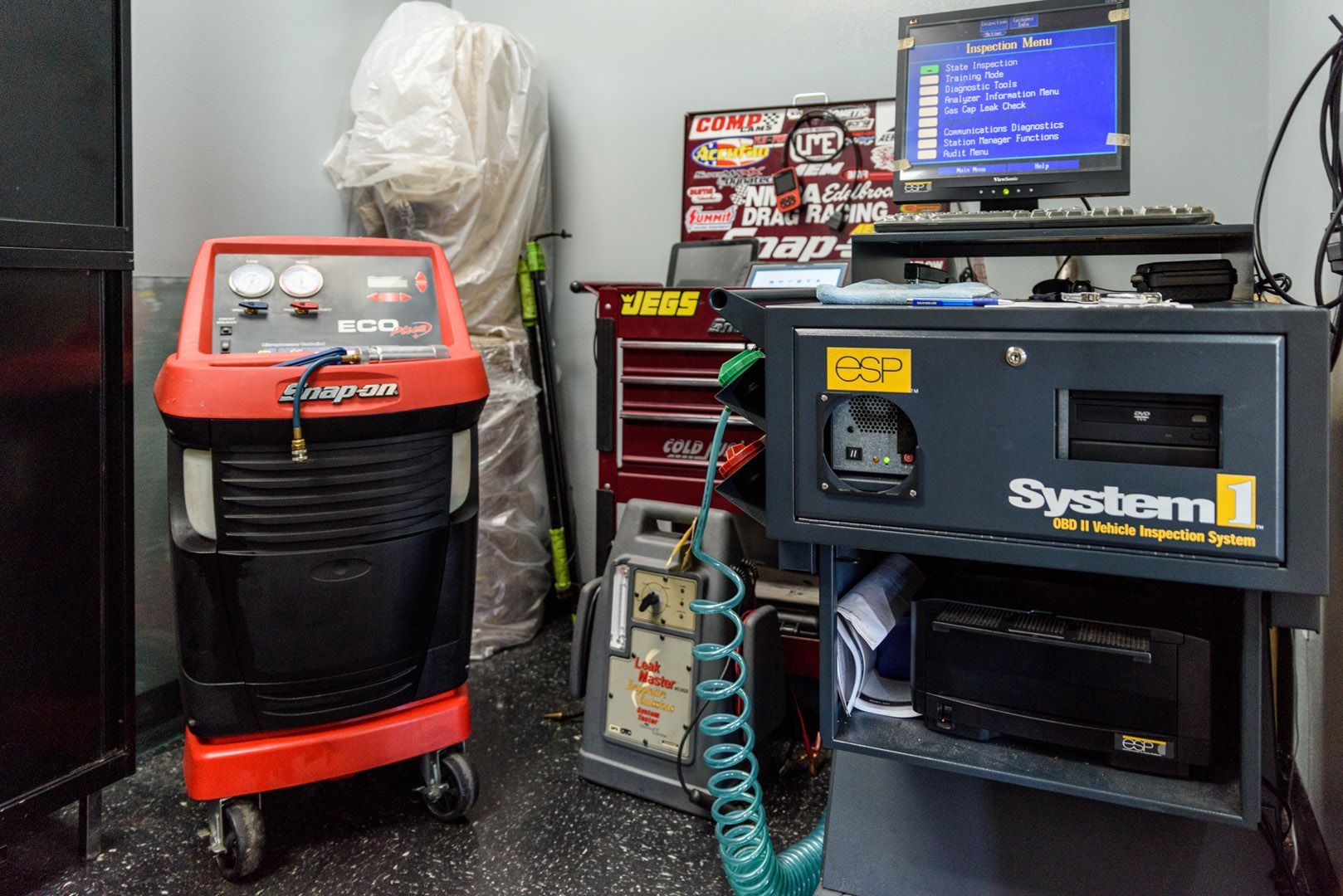 Garage workshop with a red machine, blue system unit, coiled hose, and monitor on a cart.
