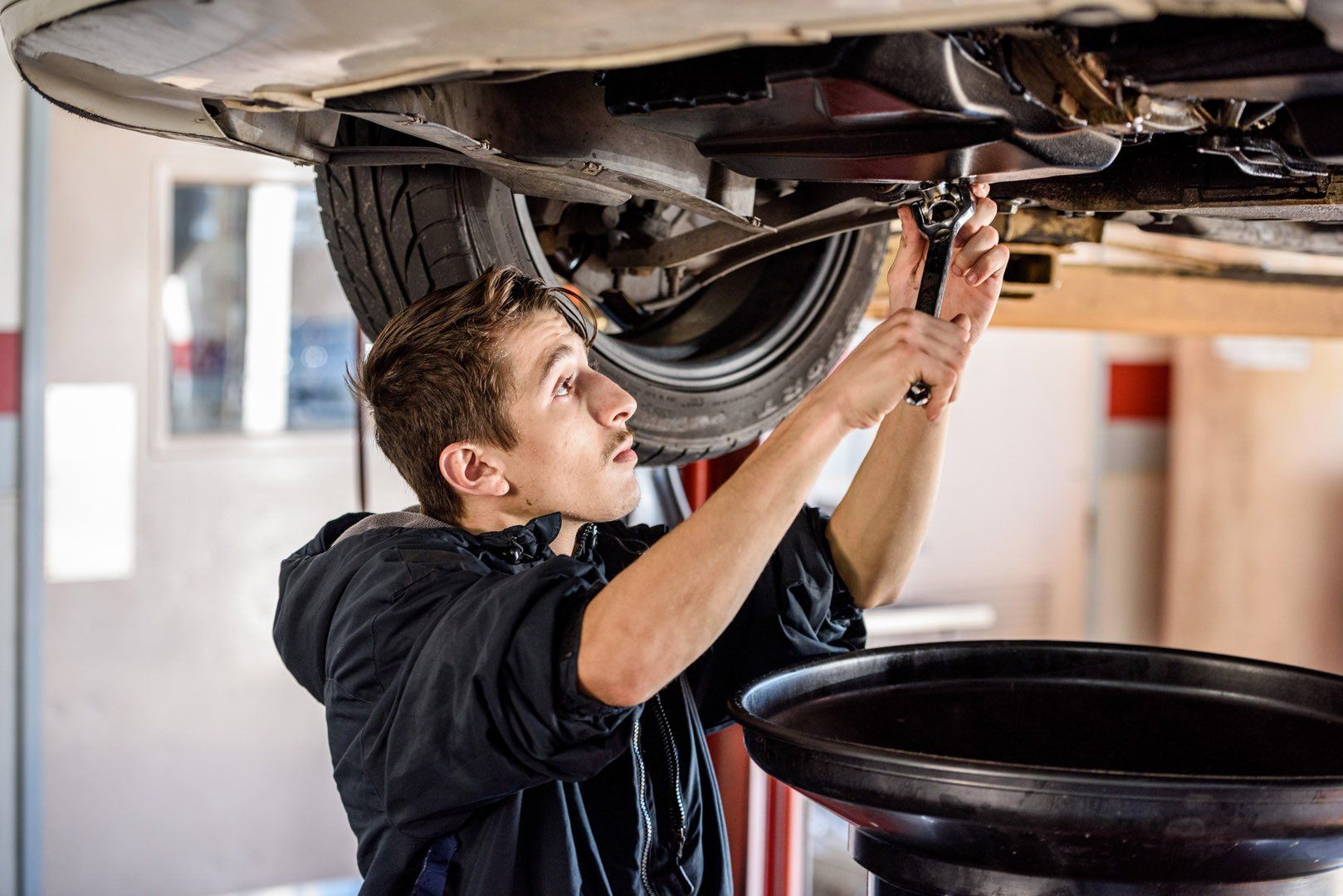 Mechanic working on the underside of a car, using a wrench to remove a bolt; oil drain pan.