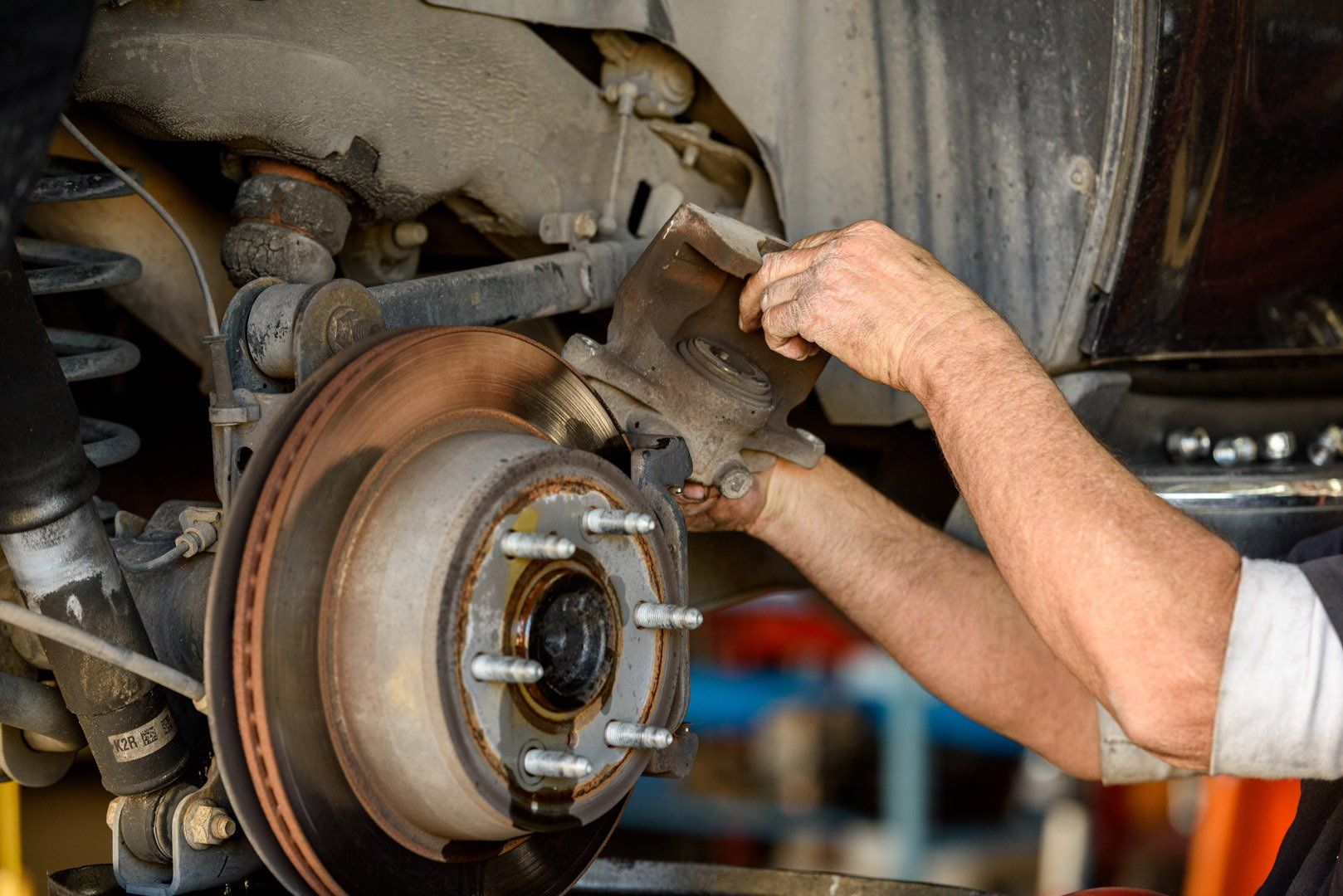 Mechanic working on car brake system, hands holding part near rotor. Dirty setting.