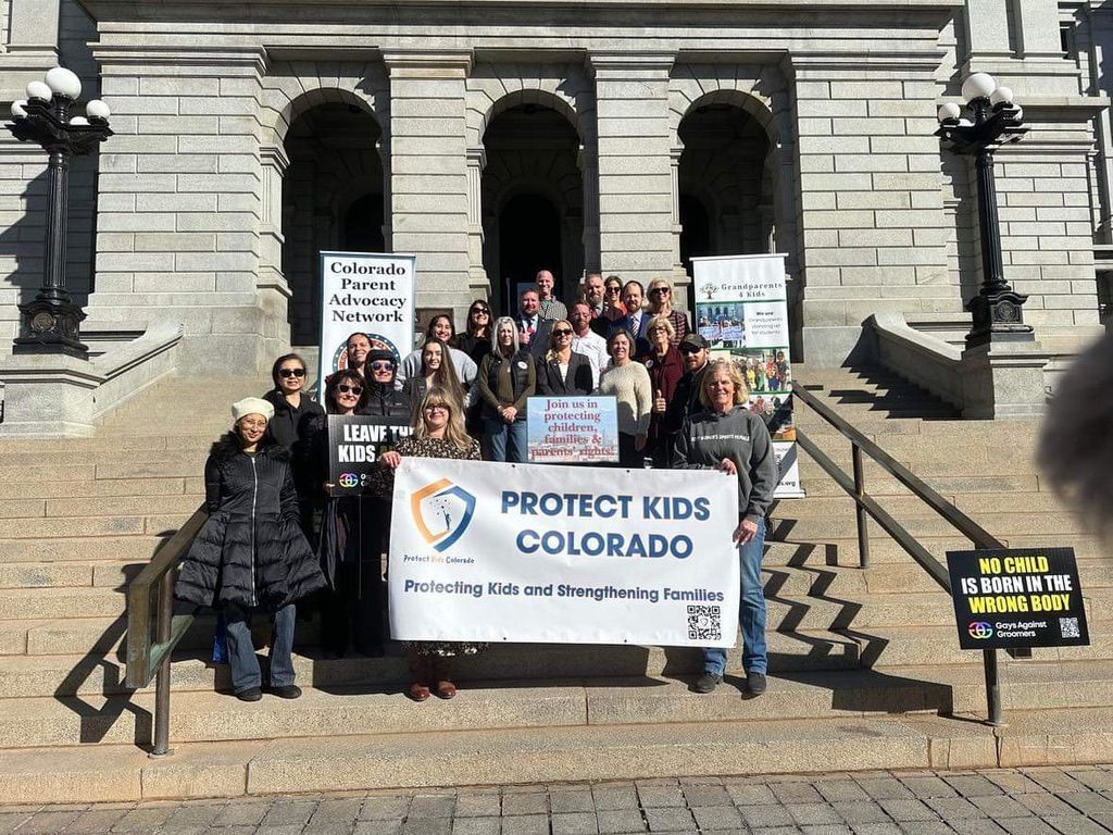 A group of people are standing in front of a building holding a sign that says protect kids colorado.