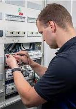 Technicus die een elektrisch schakelpaneel in een werkplaats aansluit, kabels en stroomonderbrekers afstelt.