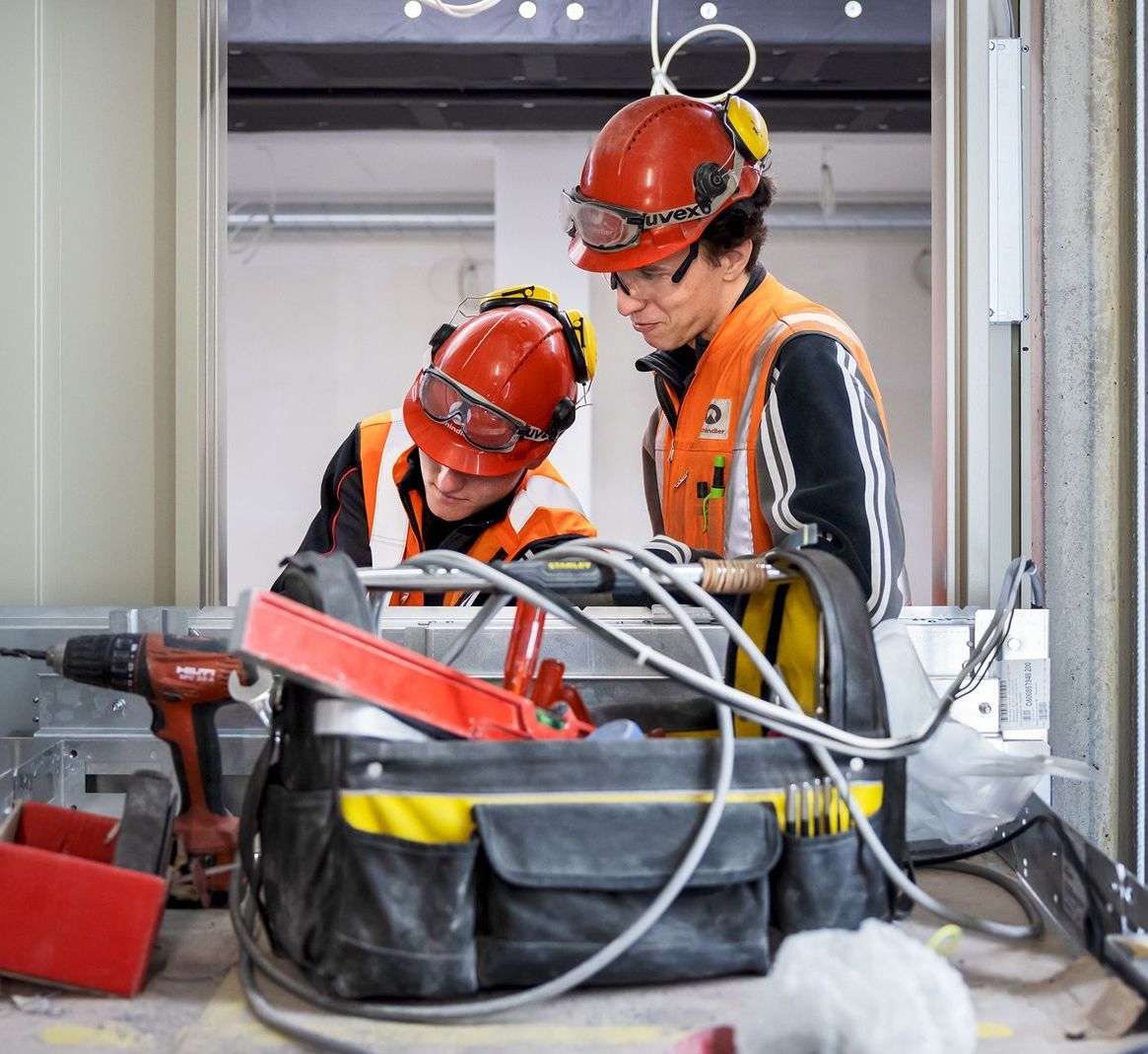 Twee bouwvakkers met oranje veiligheidshelmen inspecteren de bedrading op een bouwterrein.
