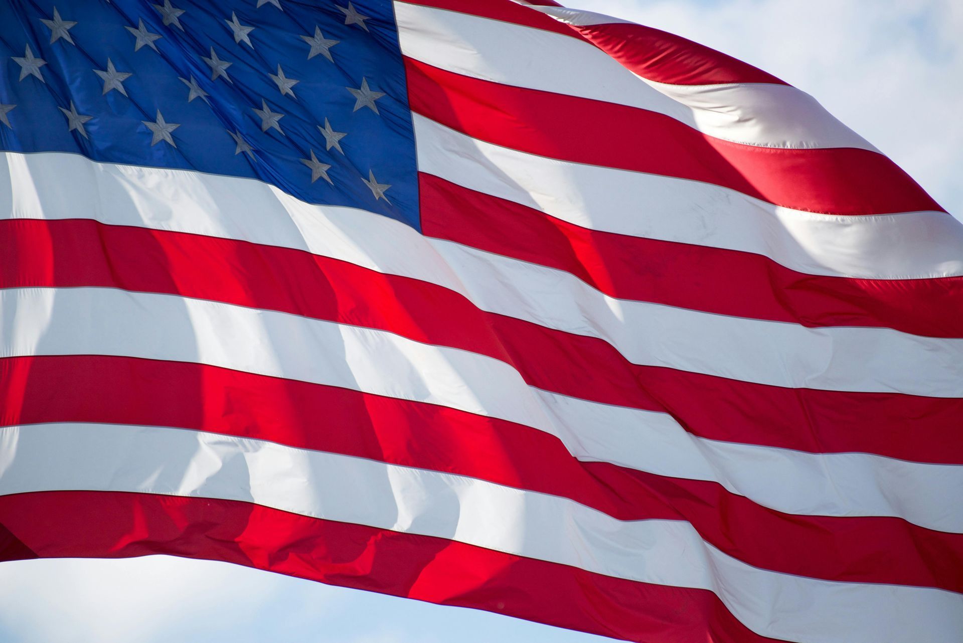 Waving American flag with red, white, and blue stripes and stars against the sky