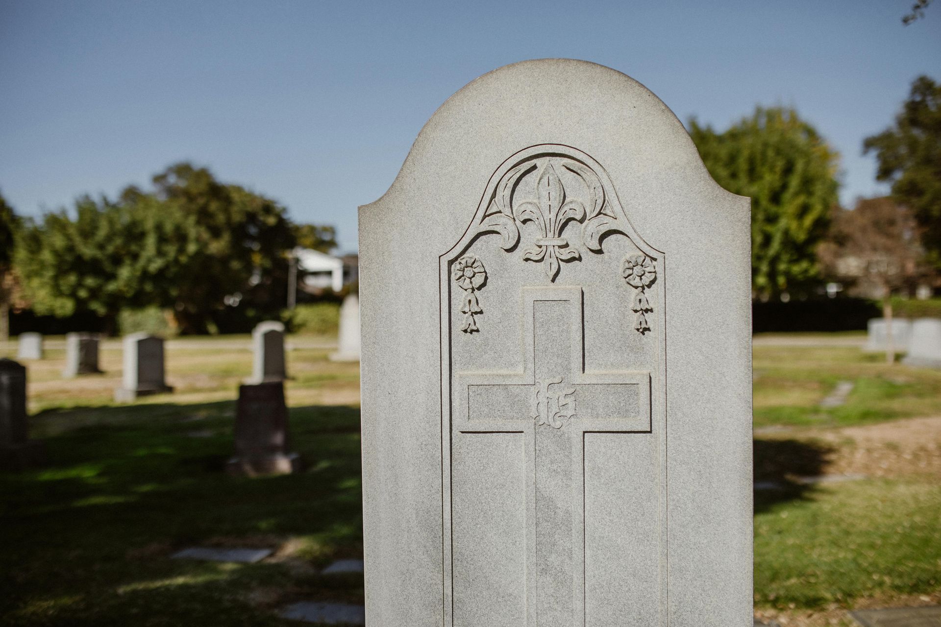 Gravestone in a cemetery, with a carved cross and floral engraving on a gray headstone.