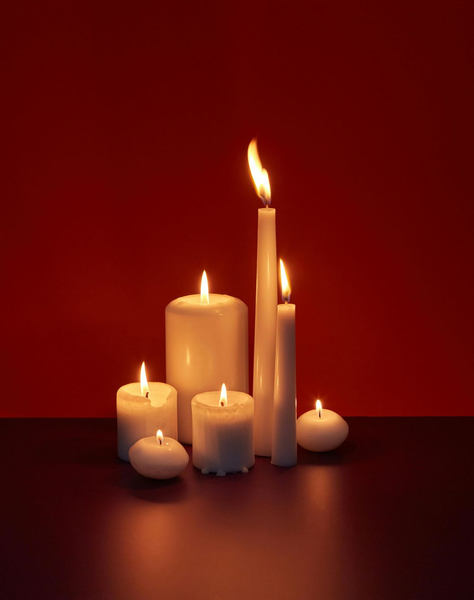 Lit white candles of varying heights on a dark red background.