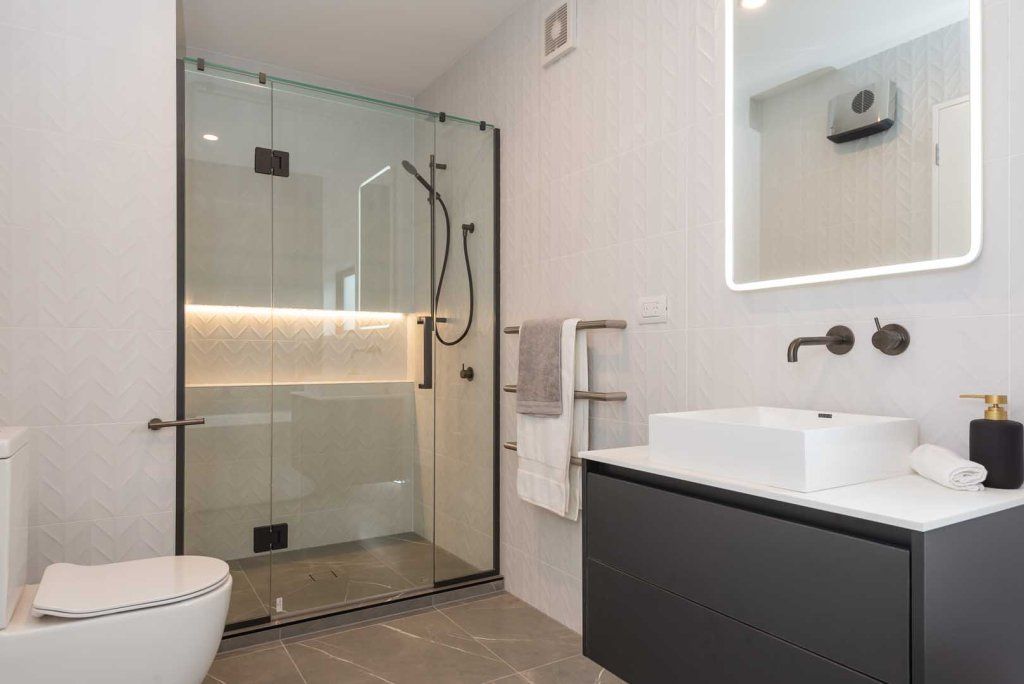 A bathroom with a toilet , sink , mirror and walk in shower.