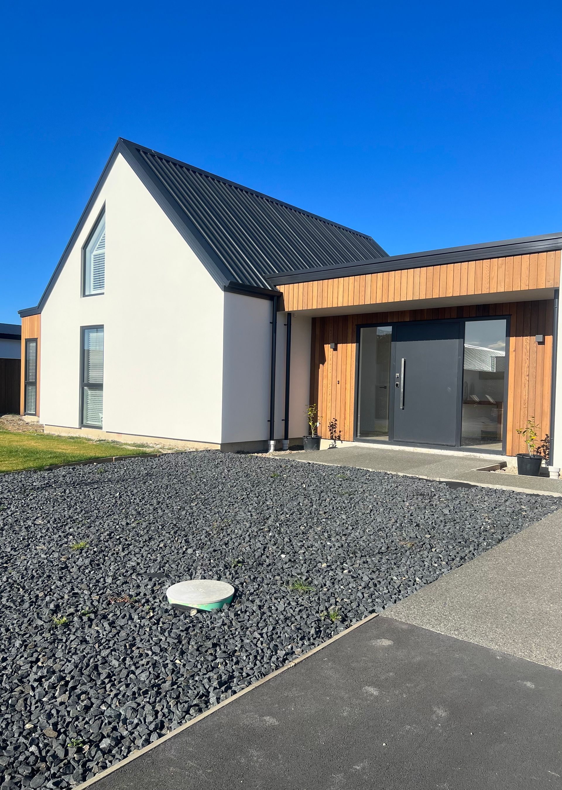A white house with a black roof is sitting next to a gravel driveway.