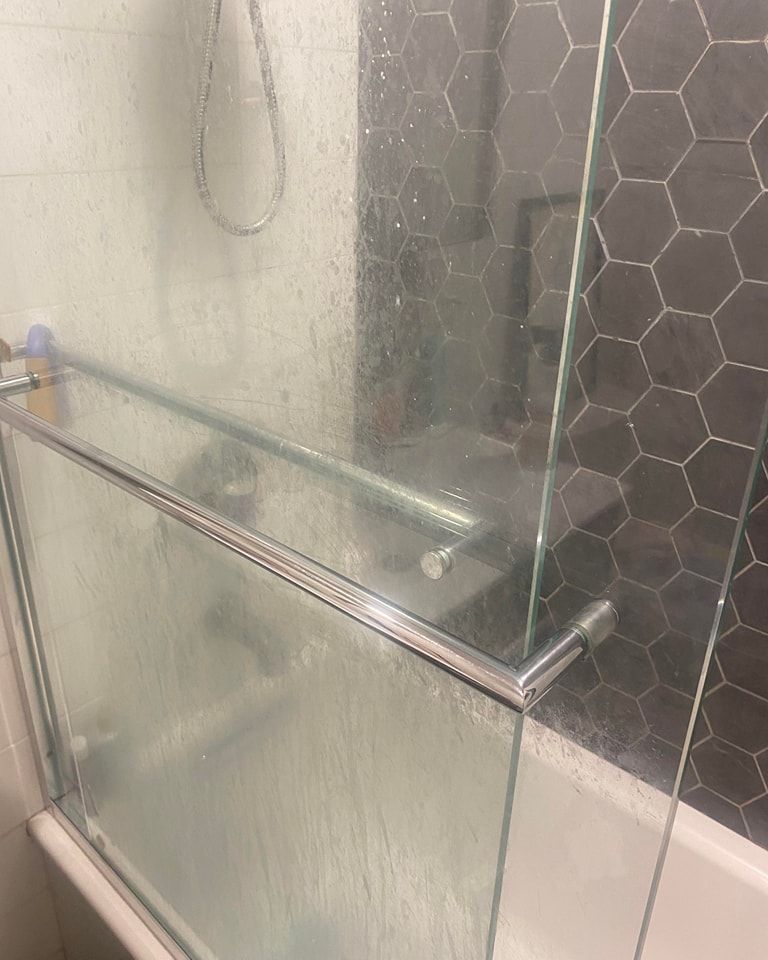 Glass shower door with chrome hardware, against dark hexagon tile wall.