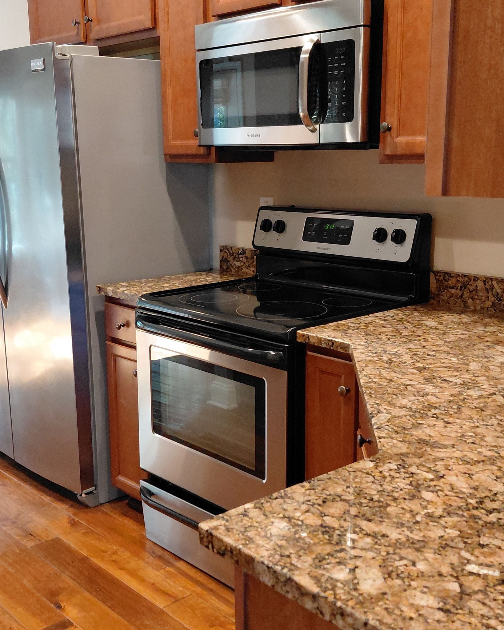 Stainless steel kitchen appliances: fridge, stove, and microwave, with granite countertops and wood cabinets.