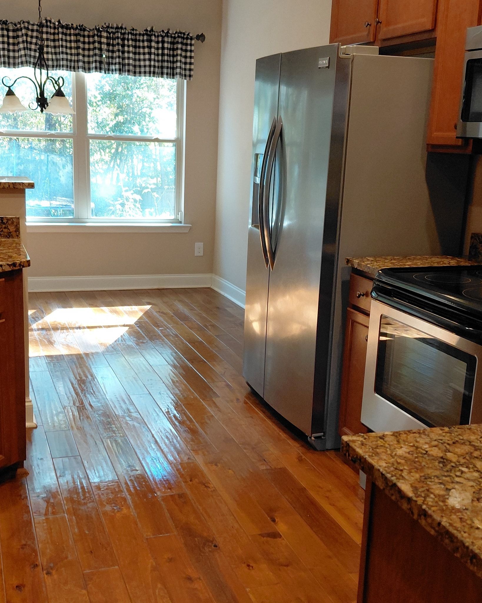 Kitchen with hardwood floors, stainless steel refrigerator, and oven. Sunlight through the window.