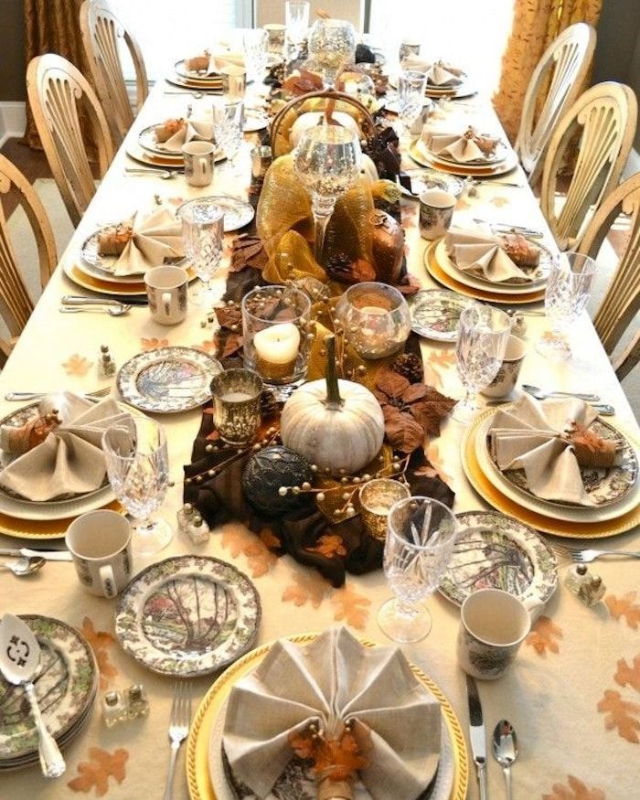 Long dining table set for Thanksgiving, featuring pumpkins, fall foliage, and elegant place settings.