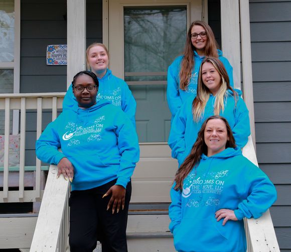Five people in blue hoodies stand on steps in front of a house.